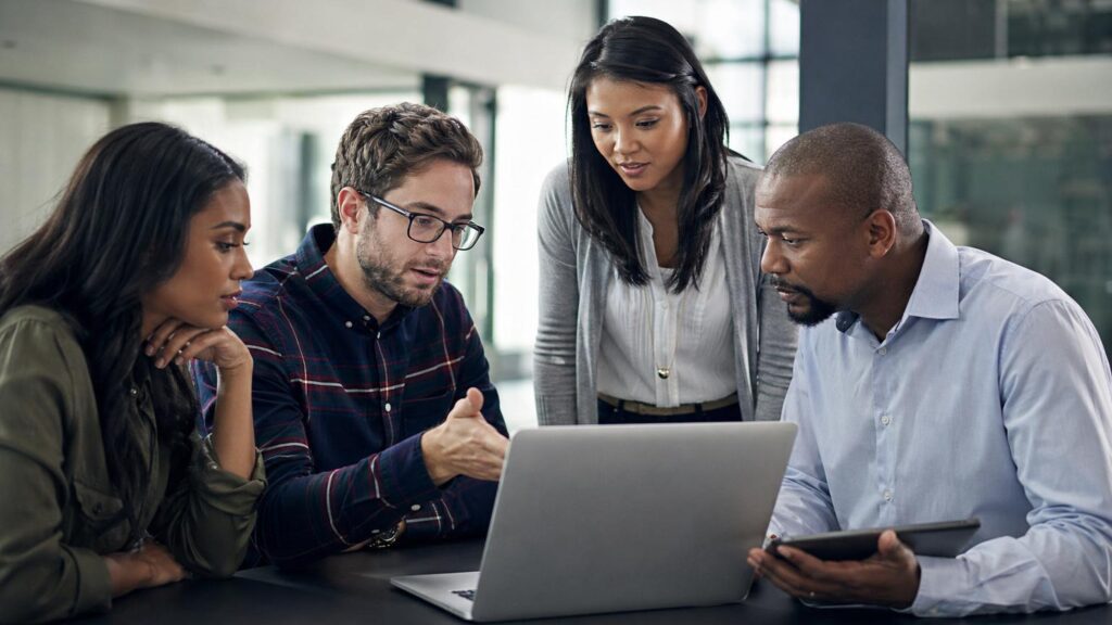 A professional team collaborating around a laptop in a modern open-plan office, illustrating how digital dexterity enables employees to adapt tools and drive organizational transformation.